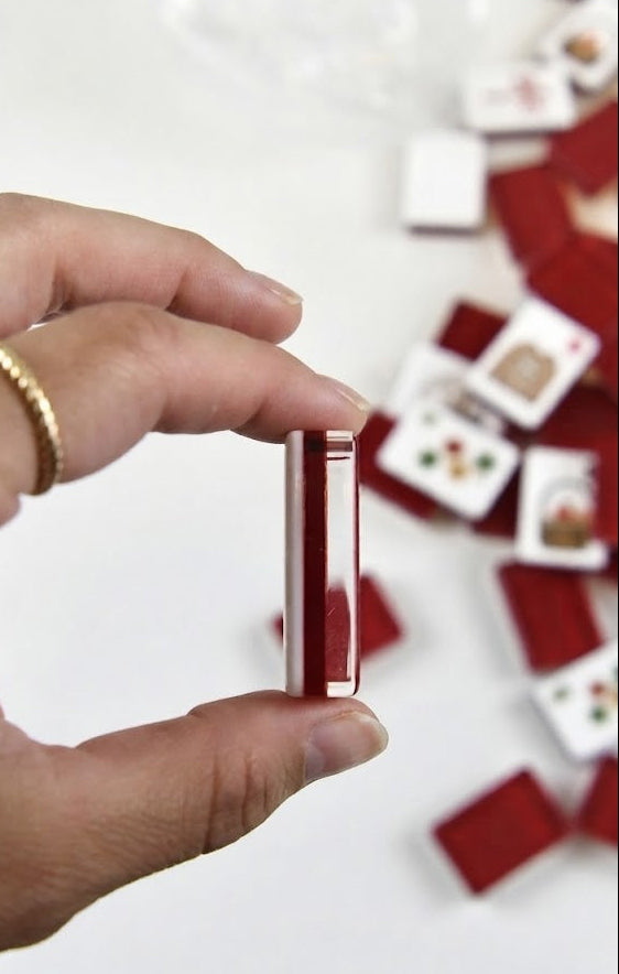 A hand holding a small red and white rectangular card or tile, with several similar cards scattered on a white surface in the background.