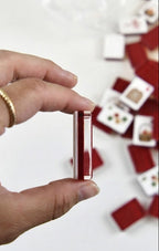 A hand holding a small red and white rectangular card or tile, with several similar cards scattered on a white surface in the background.